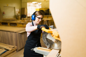 Female worker using a bench saw and wearing protective equipment