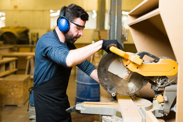 Side view of an hispanic man using a saw with protective equipment