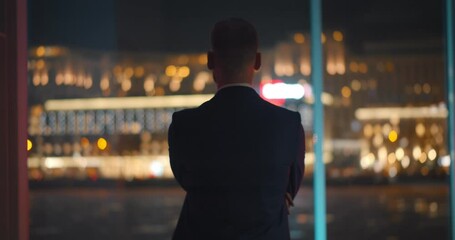 Back view of successful young businessman in suit is looking out of panoramic window. - Powered by Adobe