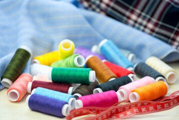 Set of colorful sewing threads, close-up. Fabric for sewing in the background.