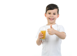 A 6-year-old boy in a white T-shirt holds a glass with citrus juice on a white background. Isolated background. Baby loves orange juice. Positive emotions. healthy food for children, schoolchildren