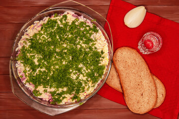 Russian holiday salad-herring under a fur coat on a wooden table with slices of bread and a glass of vodka. Step-by-step preparation of a festive dish.