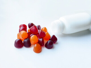 Group of red, orange and purple multivitamin gummies with the bottle isolated on white background....