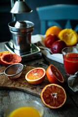 Blood orange halves with fresh juice in glasses and juicer machine on background on wooden table.