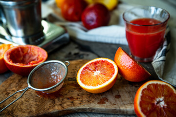 Blood orange halves with fresh juice in glasses and juicer machine on background on wooden table.