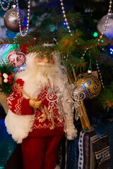 Small Santa Claus figure under beautiful decorated Christmas tree with gifts at home