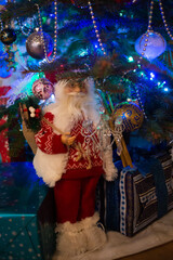 Fototapeta premium Small Santa Claus figure under beautiful decorated Christmas tree with gifts at home