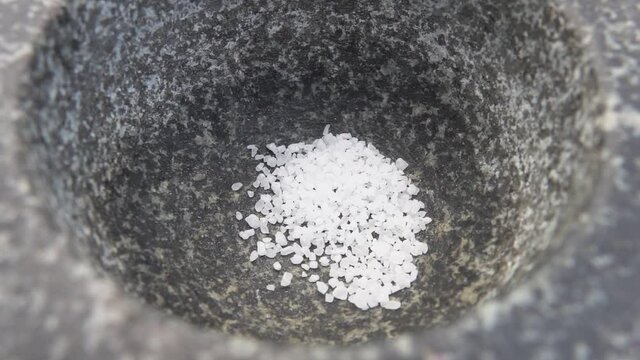 White the sea salt is falling into the grey stone mortar in slow motion