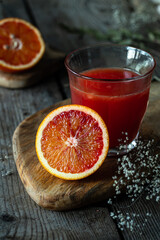 Glass of fresh blood orange juice sand blood orange half on wooden table .