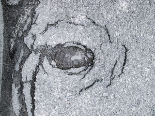 A pit on an asphalt road. A crack in the shape of a circle. The texture of the old road surface.