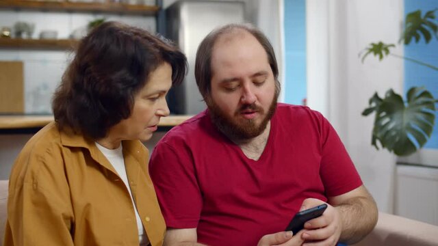 Senior mother and adult son with smartphone networking at home