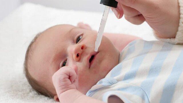 Closeup of mother giving vitamin D and K to her newborn baby son from eyedropper. Concept of babies and newborn vaccination and healthcare. Caring parents with little children.