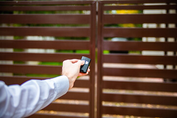 A male hand pushing a button on a remote control to open an entrance gate.