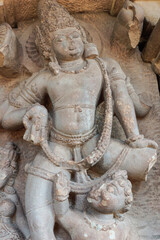 Fototapeta na wymiar Aihole, Karnataka, India - November 7, 2013: Durga Gudi or Temple. Closeup of gray stone, heavily damaged male god statue.