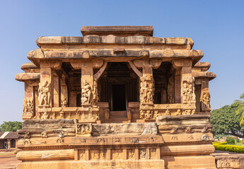 Obraz premium Aihole, Karnataka, India - November 7, 2013: Durga Gudi or Temple. Front entrance and mandapam in warm brown stones under blue sky. Green foliage on the sides.
