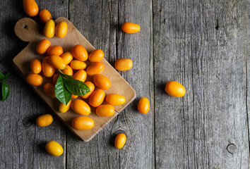 Fototapeta na wymiar Fresh ripe kumquat fruits with cutting board on wooden background, fortunella margarita