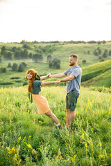 young beautiful couple red-haired girl in a pink dress and green jacket a man in a gray t-shirt and green shorts are having fun in the grass in a field in nature at sunset