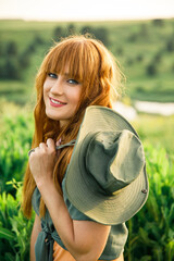 young beautiful red-haired girl in a pink dress and green jacket having fun in a field in nature at sunset