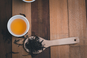 A tea cup with dry tea on the spoon and wooden background
