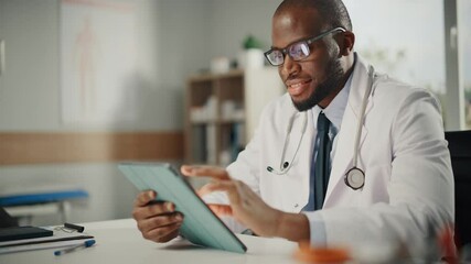 Happy and Smiling African American Male Doctor Wearing White Coat Working on Tablet Computer at His Office. Medical Health Care Professional Working with Test Results, Patient Treatment Planning. - Powered by Adobe