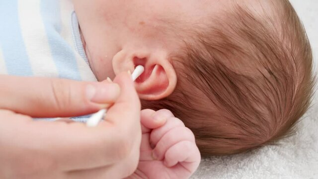 Closeup of mother using cotton swabs to clean little baby's ears from ear wax. Concept of babies and newborn hygiene and healthcare. Caring parents with little children.