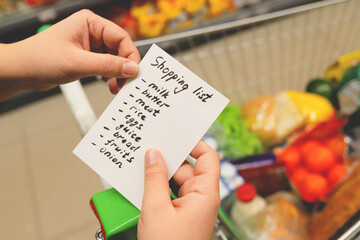 list of products in hands. supermarket with grocery cart.