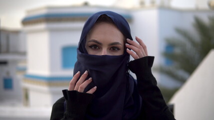 Young woman in arabic burqa. A woman looks at the camera and straightens a scarf. Against the background of the Arab house.