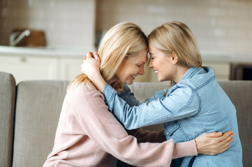 Sensual photo of aged blonde caucasian mother and her young adult happy daughter, are sitting at...