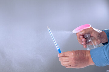 primer plano de unas manos estirilizando un esfero con un spray de alcohol gel sobre fondo gris