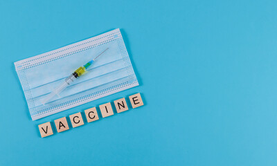 Syringe and mask.

Syringe mask and the word vaccine made from wooden cubes on a blue background with place for text on the right, top view close-up.