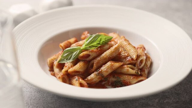 Girl pricks penne pasta with fresh green basil on a fork, close-up 