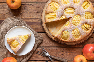 frisch gebackener Kuchen mit eingeschnittenen Äpfeln in Vierteln aus einer Springform zur Jahreszeit Frühling auf einem braunen Tisch aus Holz in der Küche