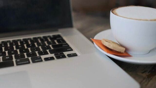 A cup of cappuccino coffee or latte coffee in a white cup with a laptop on the table. Royalty high-quality free stock footage of drink capuccino or latte coffee with a laptop for working in an office