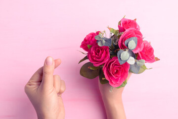Hand showing mini heart shape and holding red rose flower bouquet on pink background, Valentine day