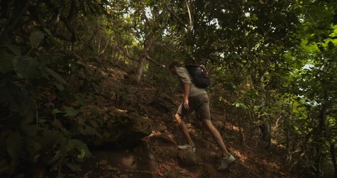 Young white male ascending up the steep hill in tropical rainforest alone. Tourist exploring a tropical jungle in Bali