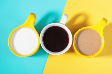 Obraz na płótnie Canvas Three mugs with coffee milk and cocoa on blue and yellow background.