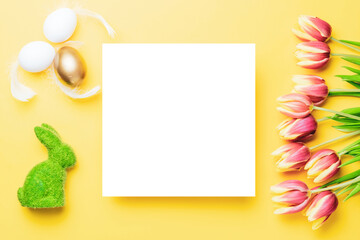 Easter background. Golden, white colour egg in basket with spring tulips, feathers on pastel yellow background in Happy Easter decoration. Spring holiday top view concept.