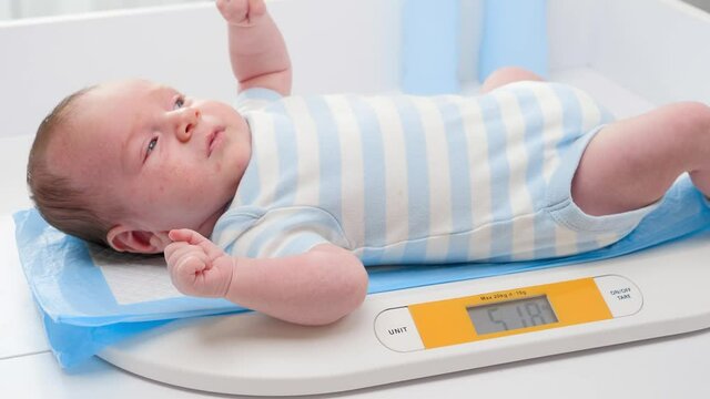 Closeup of 1 months old newborn baby boy lying on digital scales or weighs. Concept of babies and newborn hygiene and healthcare. Caring parents with little children.