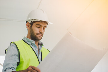 Smart young caucasian man contractor, partner holding, looking at the blueprint, inspecting the reconstructed construction and renovated after to check defect of apartment, home at site, workplace.