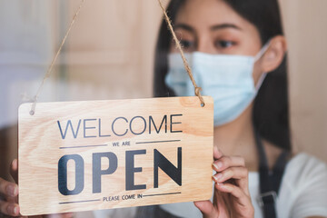 Owner retail,coffee shop woman turning sign board to open with wearing face mask ,protection to...