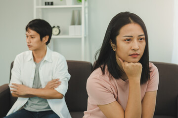 Unhappy asian young couple fights on couch, relationship is in trouble. Different people are angry and use emotions at each other. Wife has an expression of disappointment and upset with her husband.