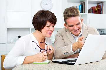 Positive son tells his mother about new software and shows his on laptop. Focus on the woman