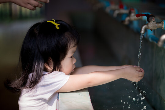 Adorable Asian little girl is washing hands with water opened by a tap. To keep the palm clean and eliminate germs and viruses. Baby age 3 years old.