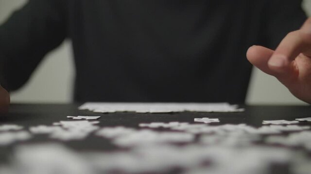 Slow Motion: Young man's hands taking a puzzle piece, trying to solve a puzzle, while more pieces are laying around on a dark table. Shot in 4K, Slow Motion with Shallow Depth of Field.	