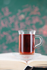 A book in front of the blackboard and a cup of tea on it