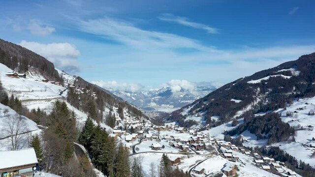 Amazing drone flight of a stunning alpine valley, village and snow covered mountain peaks in Champery, Switzerland. A beautiful winter wonderland scenic flight on a clear blue sky day.