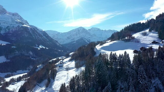 Amazing drone flight of a stunning alpine valley, village and snow covered mountain peaks in Champery, Switzerland. A beautiful winter wonderland scenic flight on a clear blue sky day.