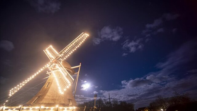 Brightly illuminated smock mill at night with moving clouds in background. Time lapse. Ameland, Friesland.