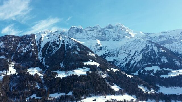 Amazing drone flight of a stunning alpine valley, village and snow covered mountain peaks in Champery, Switzerland. A beautiful winter wonderland scenic flight on a clear blue sky day.