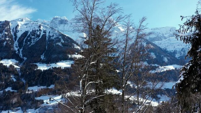 Amazing drone flight of a stunning alpine valley, village and snow covered mountain peaks in Champery, Switzerland. A beautiful winter wonderland scenic flight on a clear blue sky day.